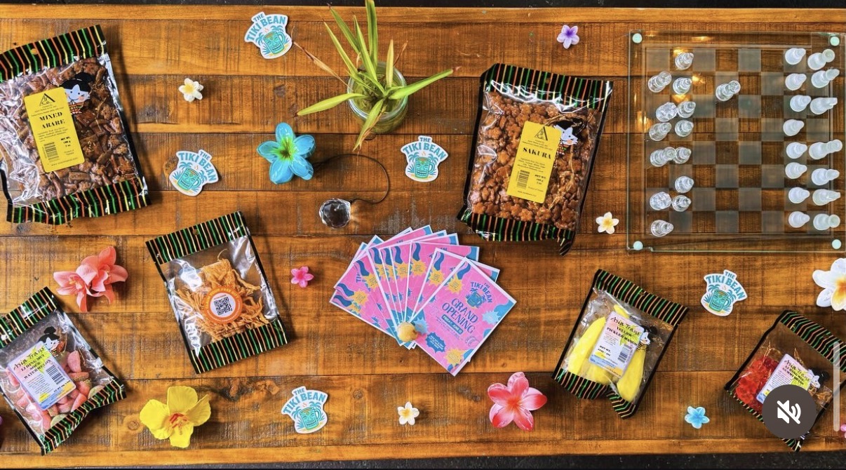 Flatlay of island snacks, stickers, flowers and grand-opening cards