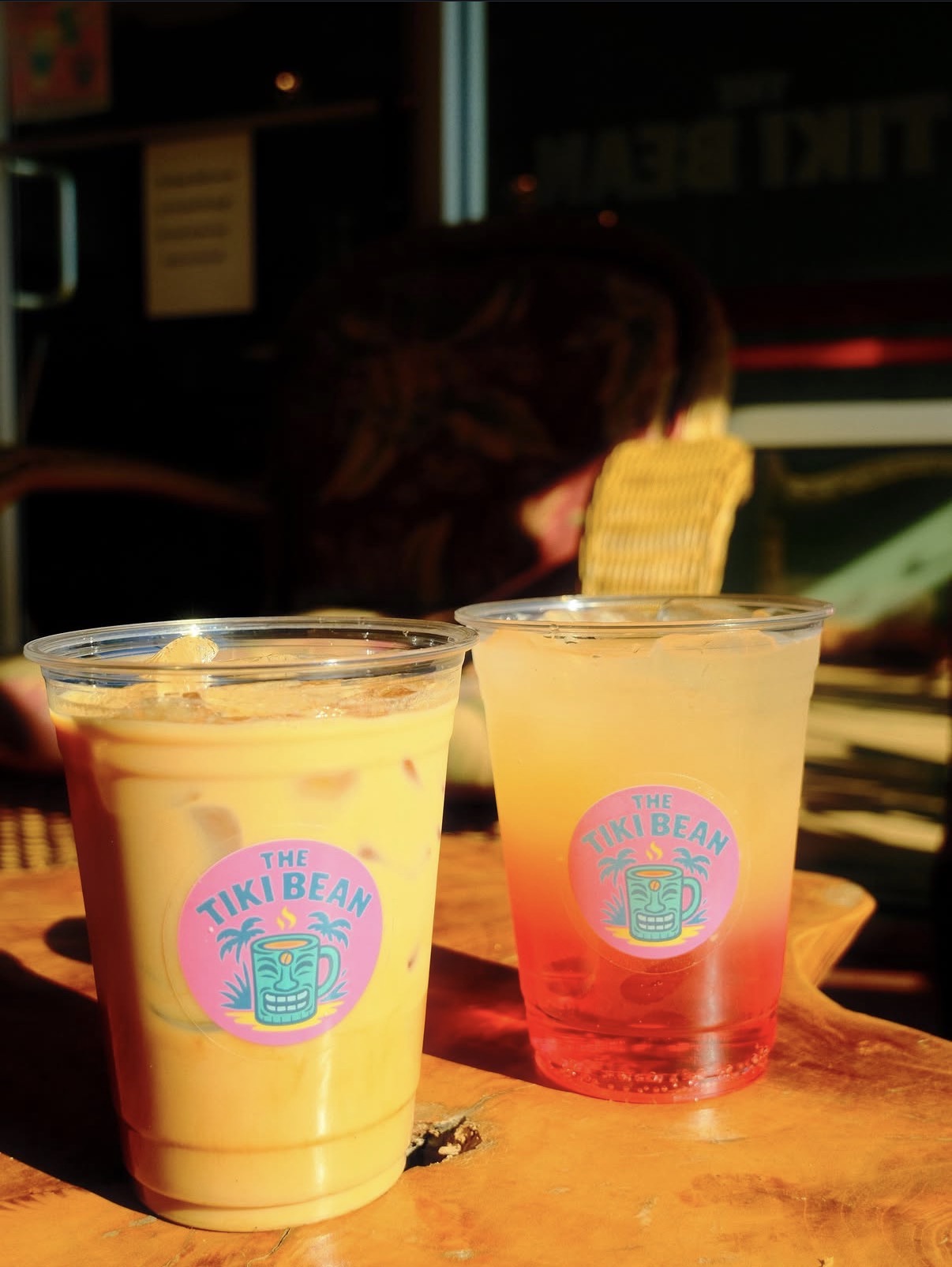Two iced Tiki Bean drinks glowing in golden-hour light in front of the shop